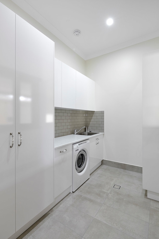 Modelo de lavadero clásico pequeño con armarios con paneles lisos, puertas de armario blancas, paredes blancas, suelo de baldosas de porcelana y suelo gris