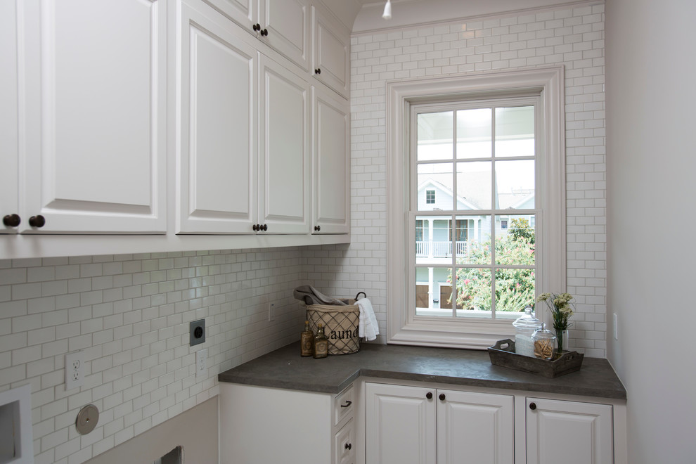 Huge elegant l-shaped dedicated laundry room photo in Houston with raised-panel cabinets, white cabinets, white backsplash, subway tile backsplash, white walls, a side-by-side washer/dryer and black countertops