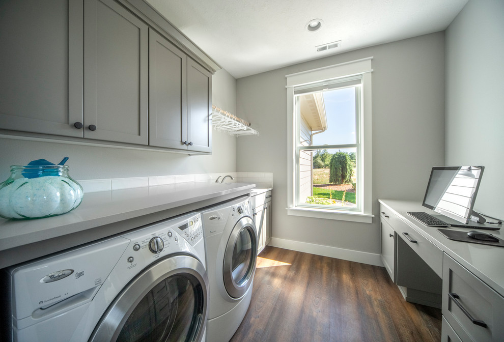 Photo of a large traditional galley utility room in Portland with a submerged sink, shaker cabinets, grey cabinets, engineered stone countertops, grey walls, medium hardwood flooring, a side by side washer and dryer, brown floors and white worktops.
