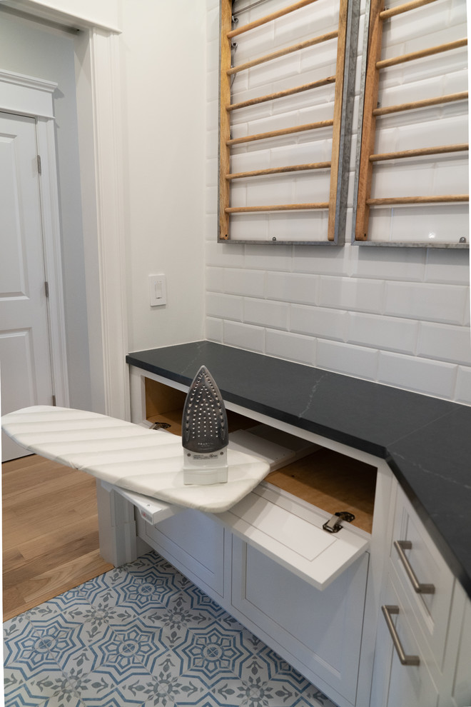 Medium sized classic u-shaped separated utility room in DC Metro with a submerged sink, recessed-panel cabinets, white cabinets, soapstone worktops, vinyl flooring, a stacked washer and dryer, multi-coloured floors and grey worktops.