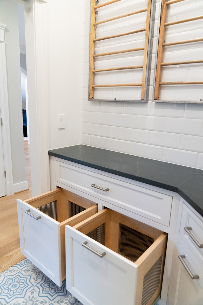 Medium sized traditional u-shaped separated utility room in DC Metro with a submerged sink, recessed-panel cabinets, white cabinets, soapstone worktops, vinyl flooring, a stacked washer and dryer, multi-coloured floors and grey worktops.
