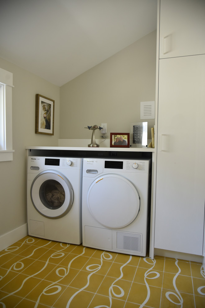 デンバーにあるラグジュアリーな中くらいなトランジショナルスタイルのおしゃれな洗濯室 (アンダーカウンターシンク、フラットパネル扉のキャビネット、白いキャビネット、クオーツストーンカウンター、グレーの壁、セラミックタイルの床、左右配置の洗濯機・乾燥機、黄色い床、白いキッチンカウンター) の写真