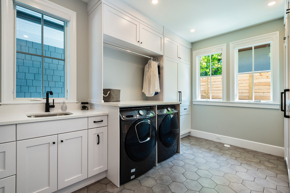 This is an example of a classic galley utility room in Vancouver with a submerged sink, shaker cabinets, white cabinets, green walls, a side by side washer and dryer, grey floors and white worktops.