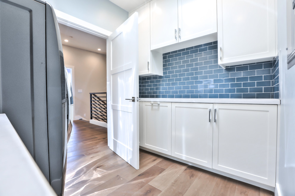 Example of a mid-sized minimalist galley medium tone wood floor dedicated laundry room design in San Francisco with an undermount sink, shaker cabinets, white cabinets, quartz countertops, blue walls, a side-by-side washer/dryer and gray countertops