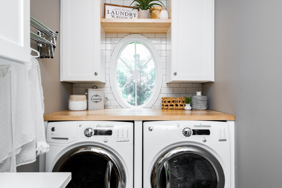 Inspiration for a small beach style single-wall utility room in St Louis with a built-in sink, flat-panel cabinets, white cabinets, wood worktops, white splashback, metro tiled splashback, grey walls, porcelain flooring, a side by side washer and dryer, grey floors and multicoloured worktops.