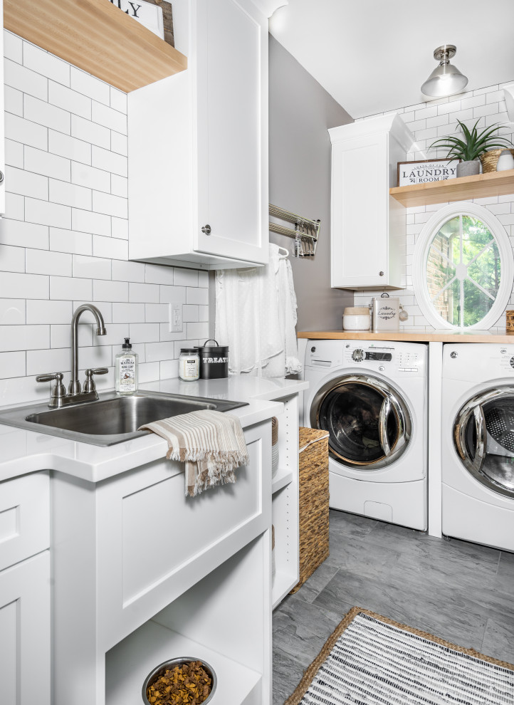 Photo of a small coastal single-wall utility room in St Louis with a built-in sink, flat-panel cabinets, white cabinets, wood worktops, white splashback, metro tiled splashback, grey walls, porcelain flooring, a side by side washer and dryer, grey floors and multicoloured worktops.