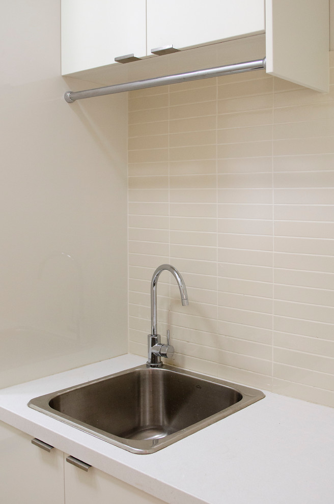 Modern inredning av en mellanstor linjär tvättstuga enbart för tvätt, med en enkel diskho, släta luckor, vita skåp, bänkskiva i kvarts, beige väggar, klinkergolv i porslin, en tvättpelare och beiget golv