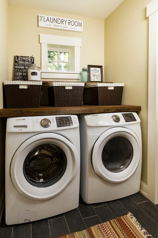ミネアポリスにある小さなトラディショナルスタイルのおしゃれな洗濯室 (I型、木材カウンター、黄色い壁、磁器タイルの床、左右配置の洗濯機・乾燥機、黒い床、茶色いキッチンカウンター) の写真