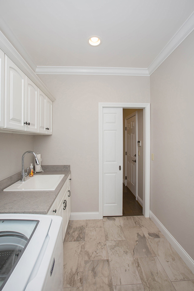 Design ideas for a medium sized traditional single-wall separated utility room in Cincinnati with a built-in sink, raised-panel cabinets, white cabinets, engineered stone countertops, grey walls, porcelain flooring, a side by side washer and dryer, beige floors and grey worktops.