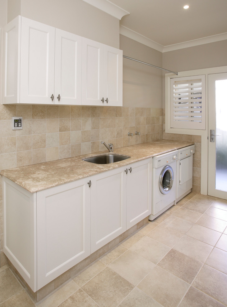 Utility room - small single-wall travertine floor utility room idea in Sydney with an undermount sink, shaker cabinets, white cabinets, marble countertops, beige walls and a side-by-side washer/dryer