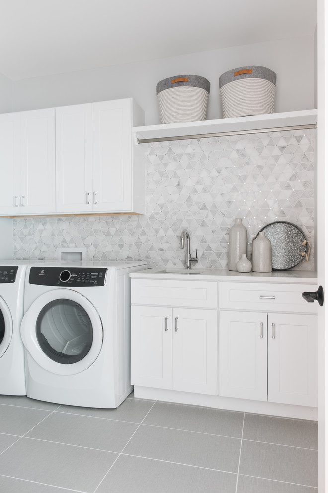 Imagen de cuarto de lavado lineal tradicional renovado con fregadero bajoencimera, armarios estilo shaker, puertas de armario blancas, paredes blancas, lavadora y secadora juntas, suelo gris y encimeras blancas
