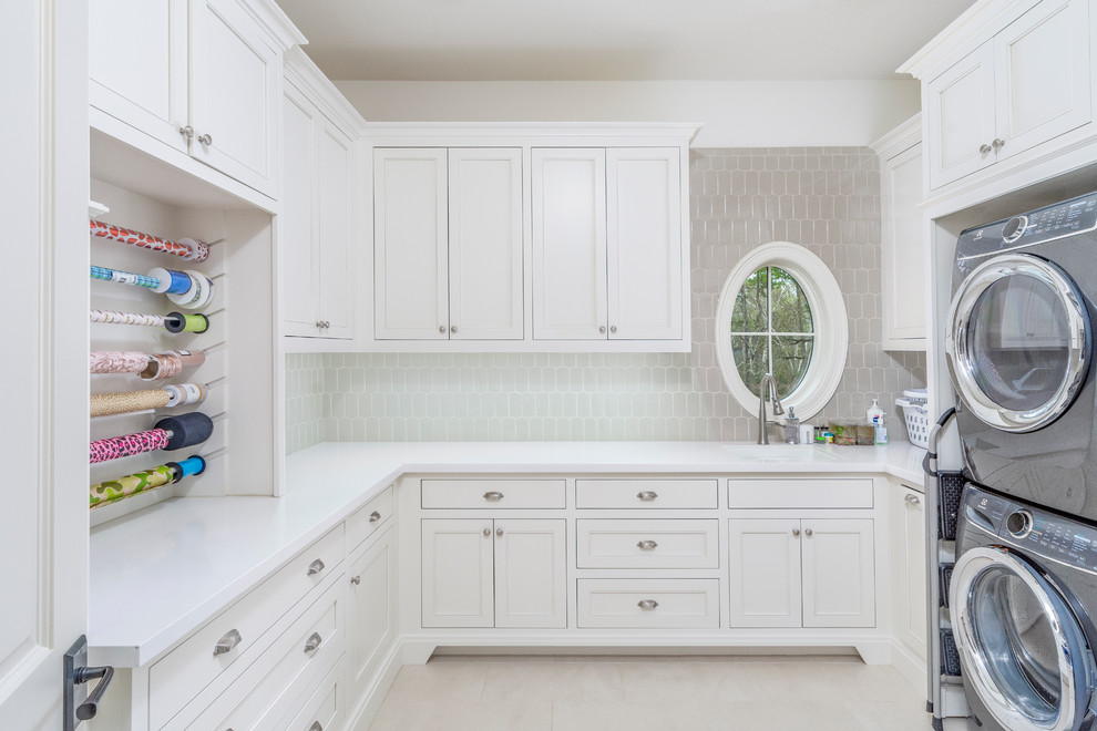 Transitional u-shaped beige floor utility room photo in Houston with an undermount sink, recessed-panel cabinets, white cabinets, white walls, a stacked washer/dryer and white countertops