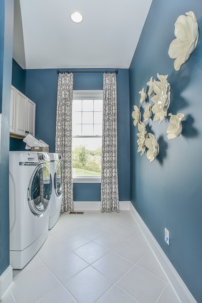 Immagine di una grande lavanderia multiuso classica con ante con bugna sagomata, ante grigie, pareti blu, pavimento con piastrelle in ceramica, lavatrice e asciugatrice affiancate e pavimento bianco