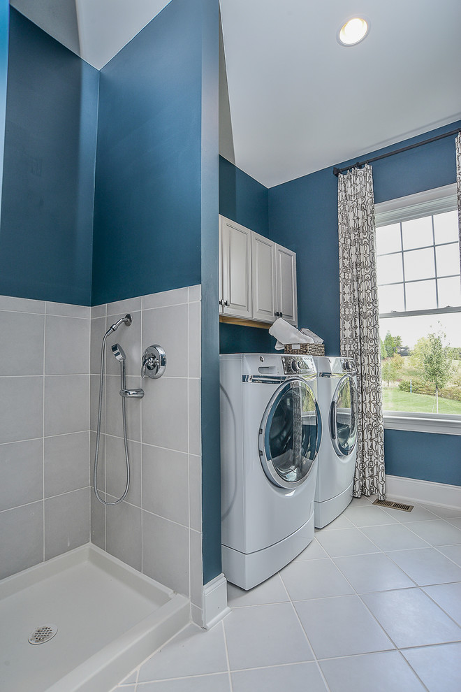 ワシントンD.C.にある高級な広いトランジショナルスタイルのおしゃれな家事室 (I型、レイズドパネル扉のキャビネット、グレーのキャビネット、青い壁、セラミックタイルの床、左右配置の洗濯機・乾燥機) の写真