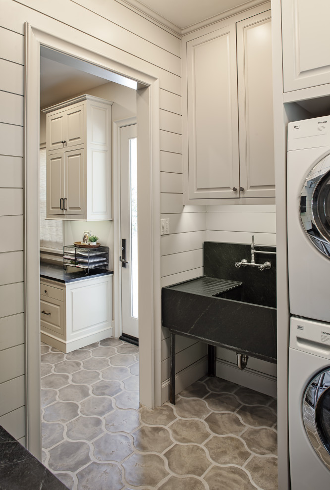 Inspiration for a medium sized classic galley separated utility room in Houston with an utility sink, raised-panel cabinets, grey cabinets, soapstone worktops, grey walls, concrete flooring, a stacked washer and dryer, grey floors and black worktops.