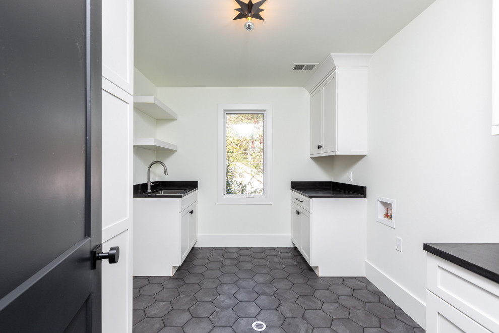 Exempel på en stor modern svarta parallell svart tvättstuga enbart för tvätt, med luckor med infälld panel, vita skåp, granitbänkskiva, vita väggar, klinkergolv i porslin och grått golv