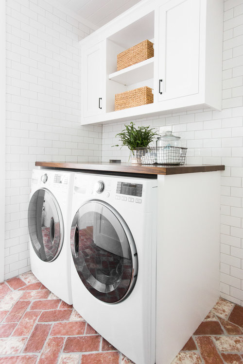 Foto de cuarto de lavado costero de tamaño medio con puertas de armario blancas, encimera de madera, paredes blancas, suelo de ladrillo, lavadora y secadora juntas, suelo rojo y encimeras marrones