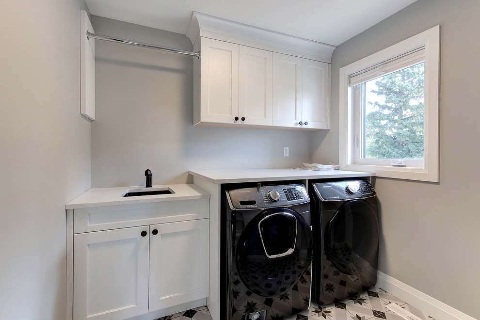 Example of a mid-sized transitional ceramic tile dedicated laundry room design in Edmonton with an undermount sink, recessed-panel cabinets, white cabinets, quartz countertops, gray walls, a side-by-side washer/dryer and white countertops