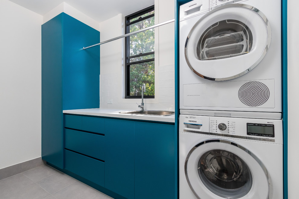 Esempio di una sala lavanderia minimalista di medie dimensioni con lavello sottopiano, ante turchesi, top in laminato, pareti grigie, lavatrice e asciugatrice a colonna, pavimento grigio e top bianco