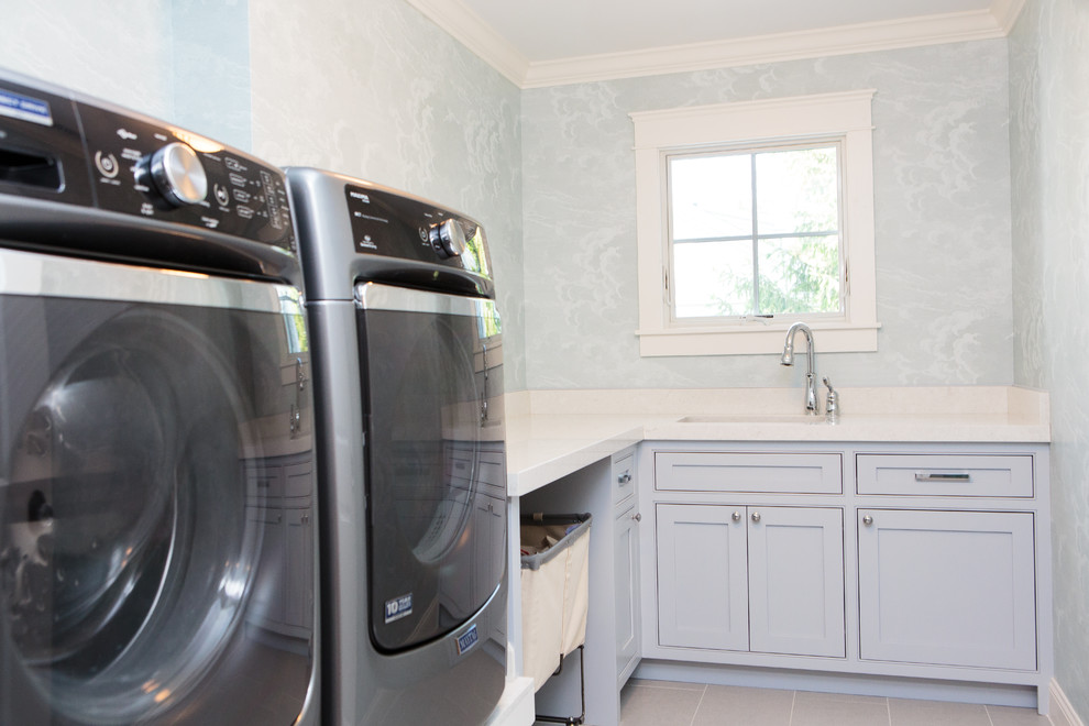 Foto di una sala lavanderia country con lavello sottopiano, ante a filo, ante blu, top in quarzo composito, pavimento con piastrelle in ceramica e lavatrice e asciugatrice affiancate