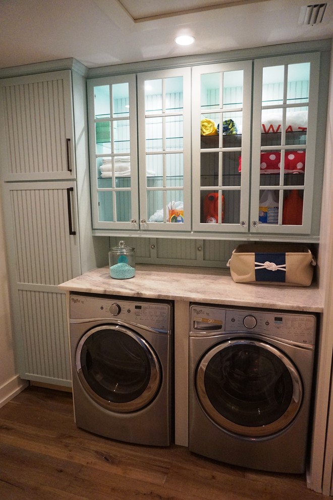 Immagine di una piccola lavanderia multiuso contemporanea con ante bianche, top in marmo, pareti blu, pavimento in legno massello medio, lavatrice e asciugatrice affiancate, pavimento marrone e ante di vetro
