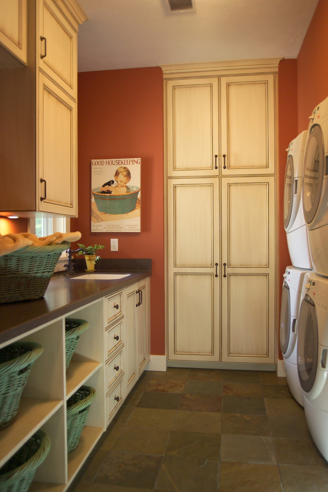 This is an example of a large traditional galley separated utility room in Grand Rapids with a submerged sink, recessed-panel cabinets, quartz worktops, orange walls, slate flooring, a stacked washer and dryer and light wood cabinets.