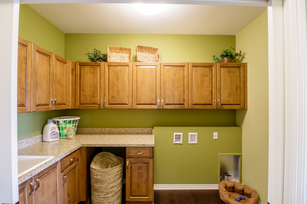 This is an example of a medium sized traditional l-shaped separated utility room in Detroit with a built-in sink, shaker cabinets, light wood cabinets, laminate countertops, green walls, medium hardwood flooring, a side by side washer and dryer and brown floors.