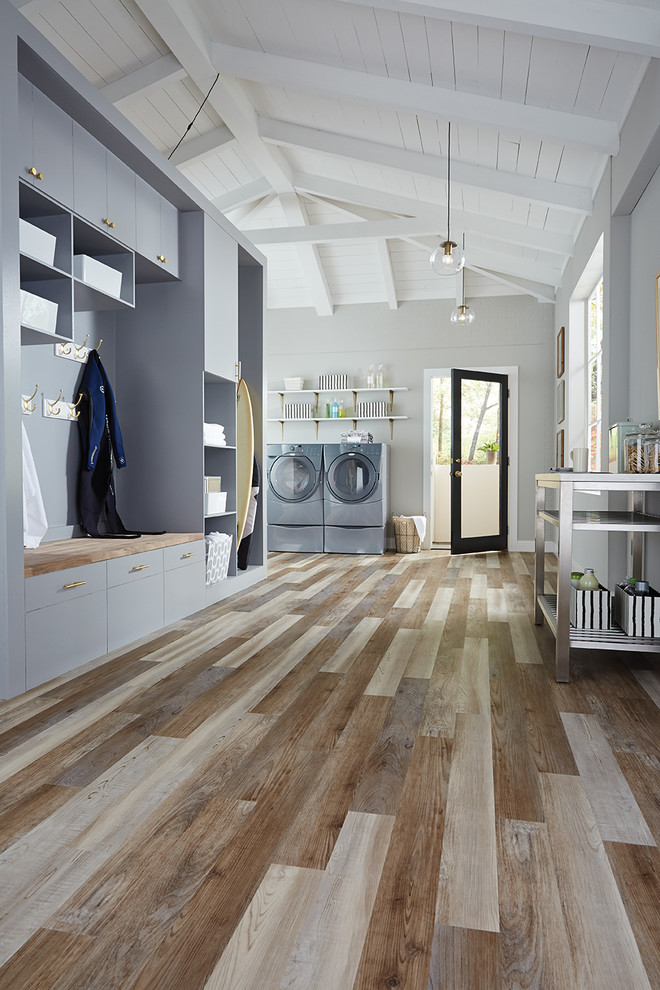 Inspiration for a large rural single-wall utility room in Tampa with flat-panel cabinets, blue cabinets, grey walls, light hardwood flooring, a side by side washer and dryer and multi-coloured floors.