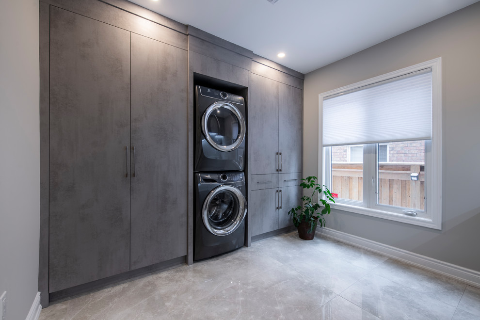 Foto de cuarto de lavado lineal actual grande con armarios con paneles lisos, paredes grises, suelo de mármol, lavadora y secadora apiladas, suelo gris y puertas de armario grises