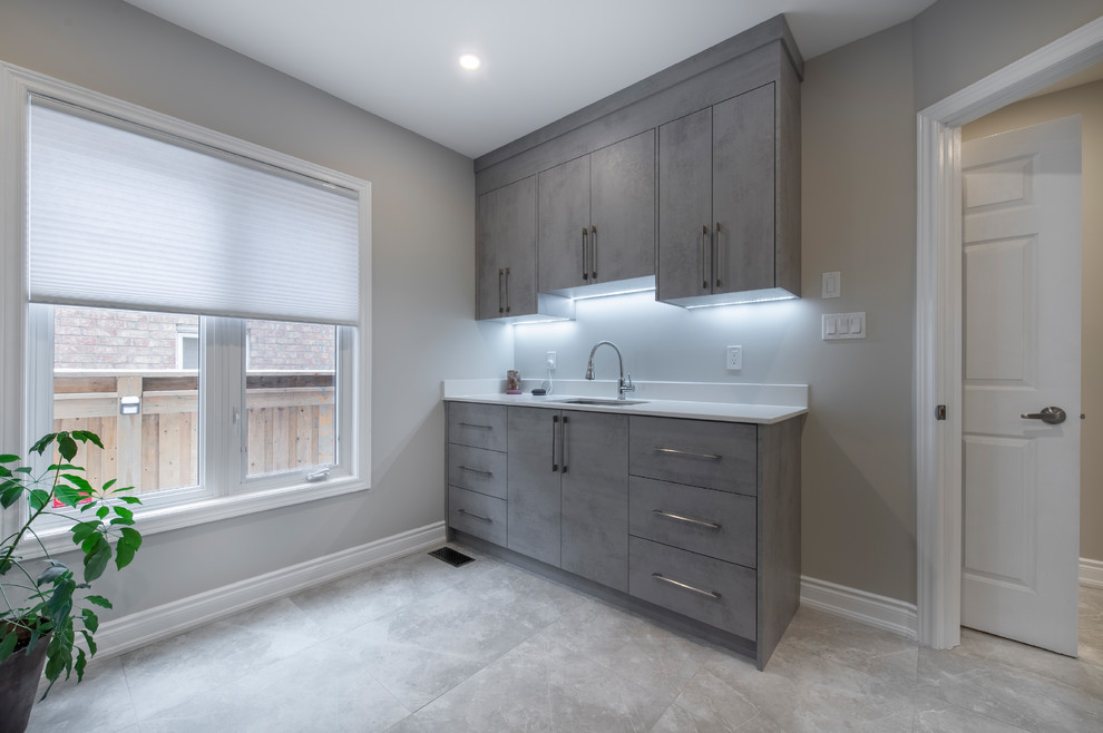 Photo of a large contemporary single-wall separated utility room in Toronto with flat-panel cabinets, grey walls, marble flooring, a stacked washer and dryer, grey floors and grey cabinets.