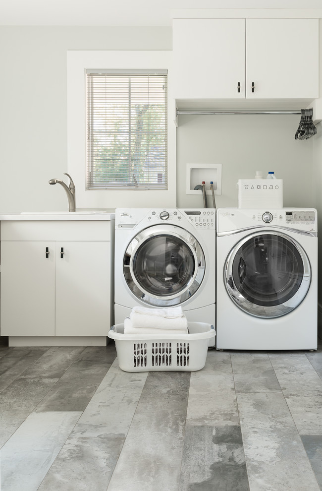 Foto på en stor funkis tvättstuga, med en nedsänkt diskho, vita skåp, vita väggar, klinkergolv i porslin, en tvättmaskin och torktumlare bredvid varandra och släta luckor