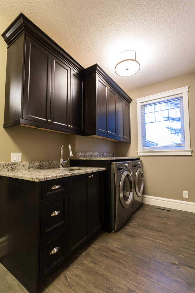 Dedicated laundry room - large craftsman single-wall porcelain tile dedicated laundry room idea in Edmonton with an undermount sink, shaker cabinets, dark wood cabinets, granite countertops, beige walls and a side-by-side washer/dryer