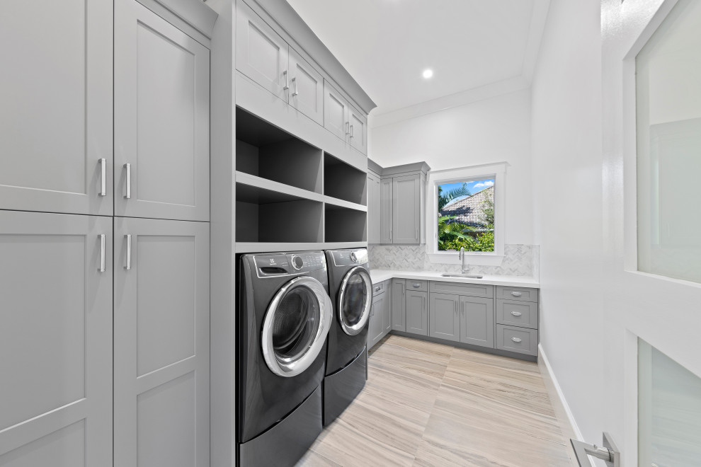 Design ideas for a large traditional l-shaped separated utility room in Miami with a submerged sink, shaker cabinets, grey cabinets, quartz worktops, white walls, porcelain flooring, a side by side washer and dryer, beige floors and white worktops.