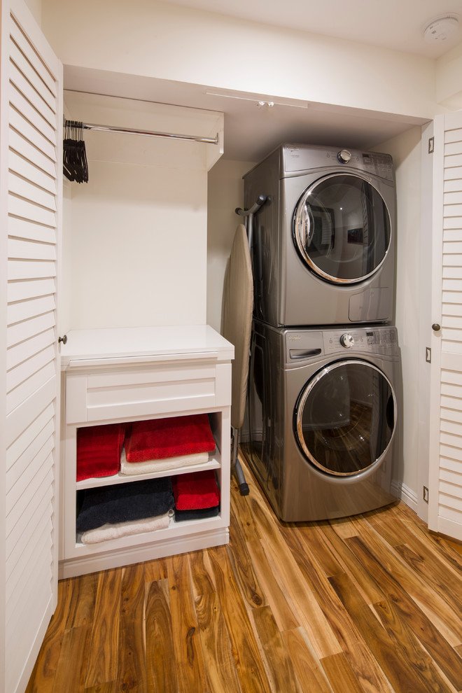 Foto de armario lavadero lineal clásico renovado de tamaño medio con armarios estilo shaker, puertas de armario blancas, paredes blancas, suelo de madera en tonos medios, lavadora y secadora apiladas y suelo marrón