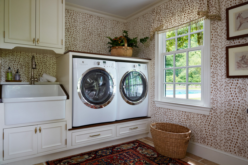 Exempel på en stor klassisk bruna brunt tvättstuga enbart för tvätt, med en allbänk, luckor med profilerade fronter, beige skåp, träbänkskiva och en tvättmaskin och torktumlare bredvid varandra