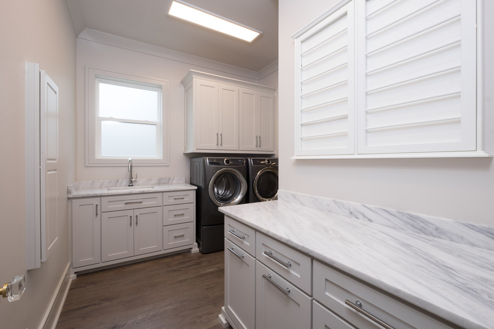 Idéer för mellanstora vintage linjära grått tvättstugor enbart för tvätt, med en undermonterad diskho, skåp i shakerstil, vita skåp, marmorbänkskiva, vita väggar, mörkt trägolv, en tvättmaskin och torktumlare bredvid varandra och brunt golv