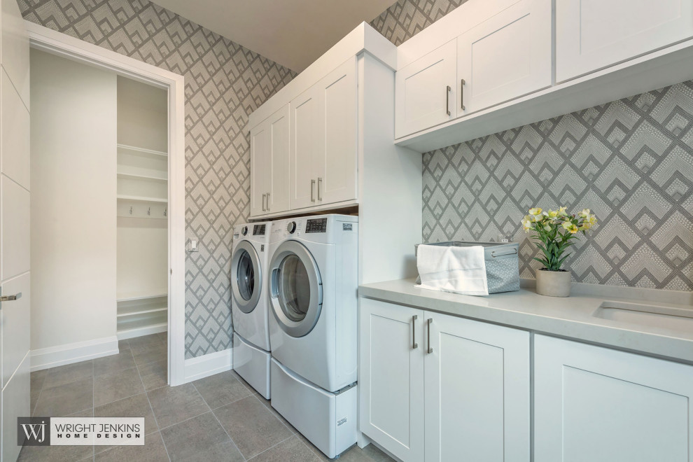 Idéer för att renovera en stor amerikansk grå parallell grått tvättstuga enbart för tvätt, med en undermonterad diskho, luckor med infälld panel, vita skåp, bänkskiva i kvarts, beige stänkskydd, stänkskydd i porslinskakel, beige väggar, skiffergolv, en tvättmaskin och torktumlare bredvid varandra och grått golv