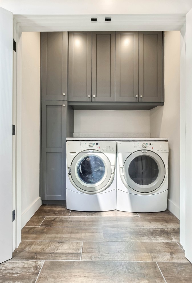 Bild på en mellanstor vintage linjär tvättstuga enbart för tvätt, med skåp i shakerstil, grå skåp, vita väggar, klinkergolv i keramik, en tvättmaskin och torktumlare bredvid varandra och brunt golv