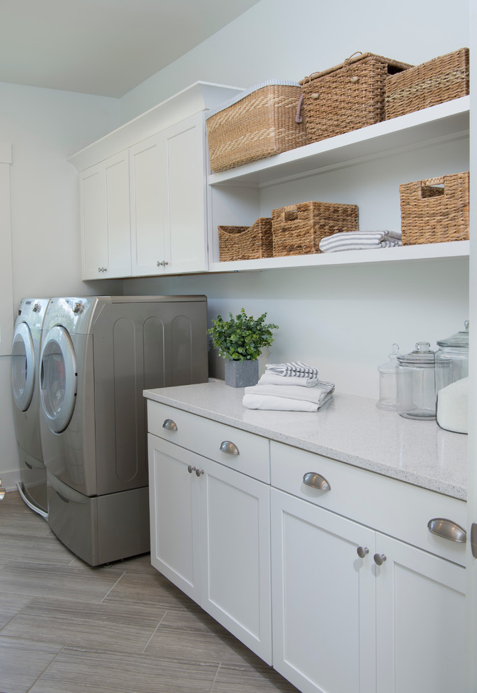 Foto på en stor lantlig linjär tvättstuga enbart för tvätt, med luckor med infälld panel, vita skåp, bänkskiva i kvarts, grå väggar, klinkergolv i keramik och en tvättmaskin och torktumlare bredvid varandra
