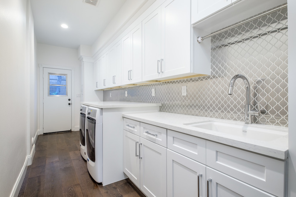 Large transitional single-wall dark wood floor and brown floor laundry room photo in Orange County with an undermount sink, shaker cabinets, white cabinets, white walls, a side-by-side washer/dryer and white countertops