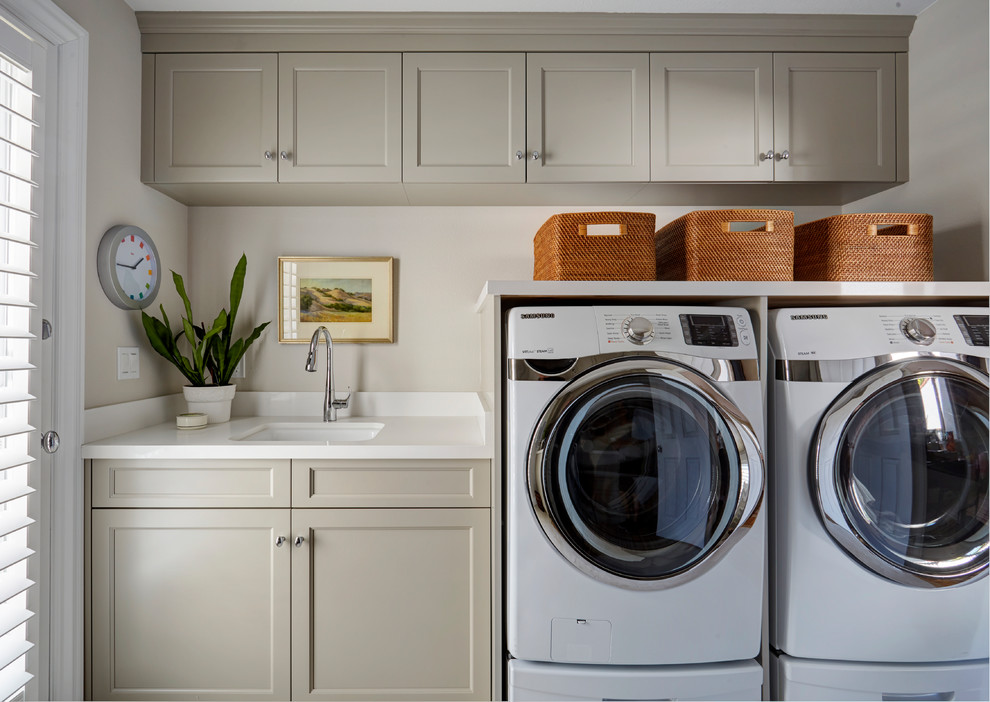 Exempel på en stor klassisk vita l-formad vitt tvättstuga enbart för tvätt, med en undermonterad diskho, luckor med infälld panel, grå skåp, bänkskiva i kvarts, beige väggar, klinkergolv i porslin, en tvättmaskin och torktumlare bredvid varandra och beiget golv