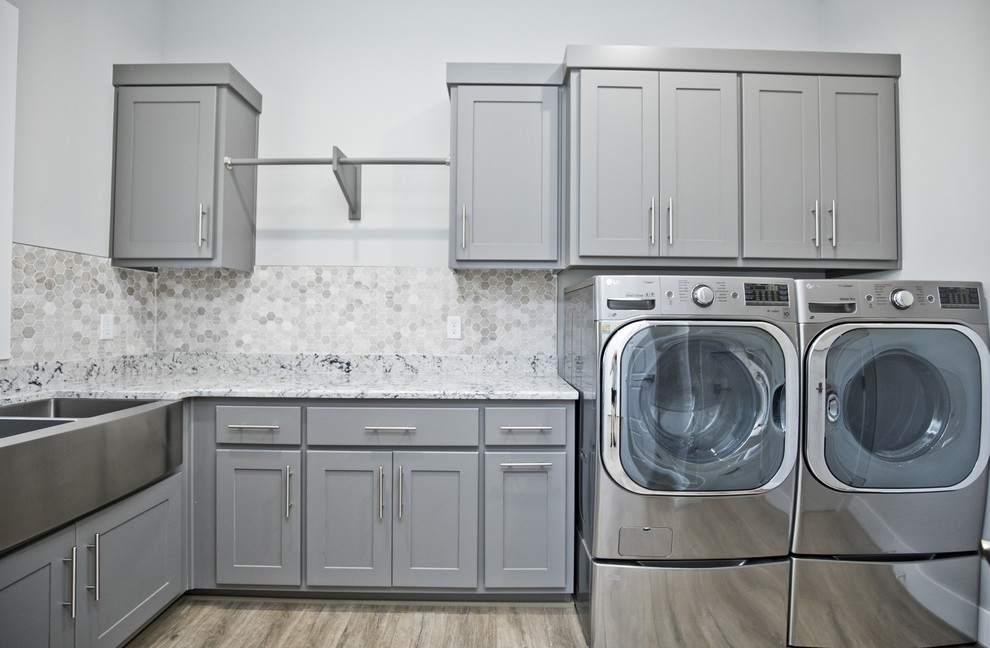 Dedicated laundry room - mid-sized contemporary single-wall medium tone wood floor and brown floor dedicated laundry room idea in Other with a farmhouse sink, recessed-panel cabinets, gray cabinets, granite countertops, gray walls, a side-by-side washer/dryer and multicolored countertops