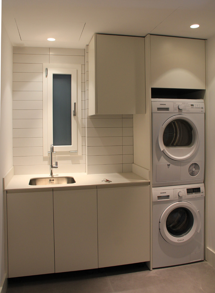 Modelo de cuarto de lavado tradicional renovado de tamaño medio con armarios con paneles lisos, puertas de armario beige, paredes blancas, lavadora y secadora apiladas y fregadero bajoencimera