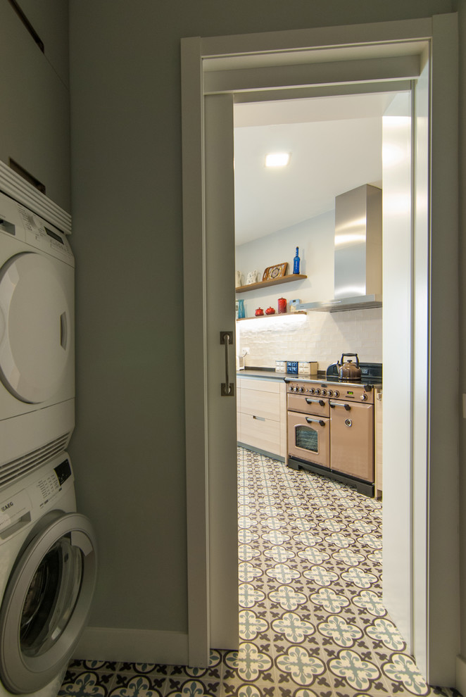 Imagen de cuarto de lavado lineal tradicional renovado pequeño con lavadora y secadora apiladas, armarios con paneles lisos y suelo de baldosas de cerámica