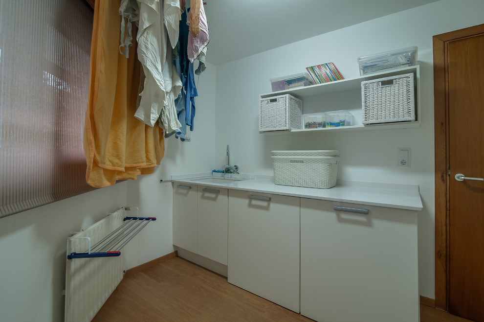 Einzeilige, Mittelgroße Klassische Waschküche mit Waschbecken, flächenbündigen Schrankfronten, weißen Schränken, weißer Wandfarbe und braunem Holzboden in Sonstige