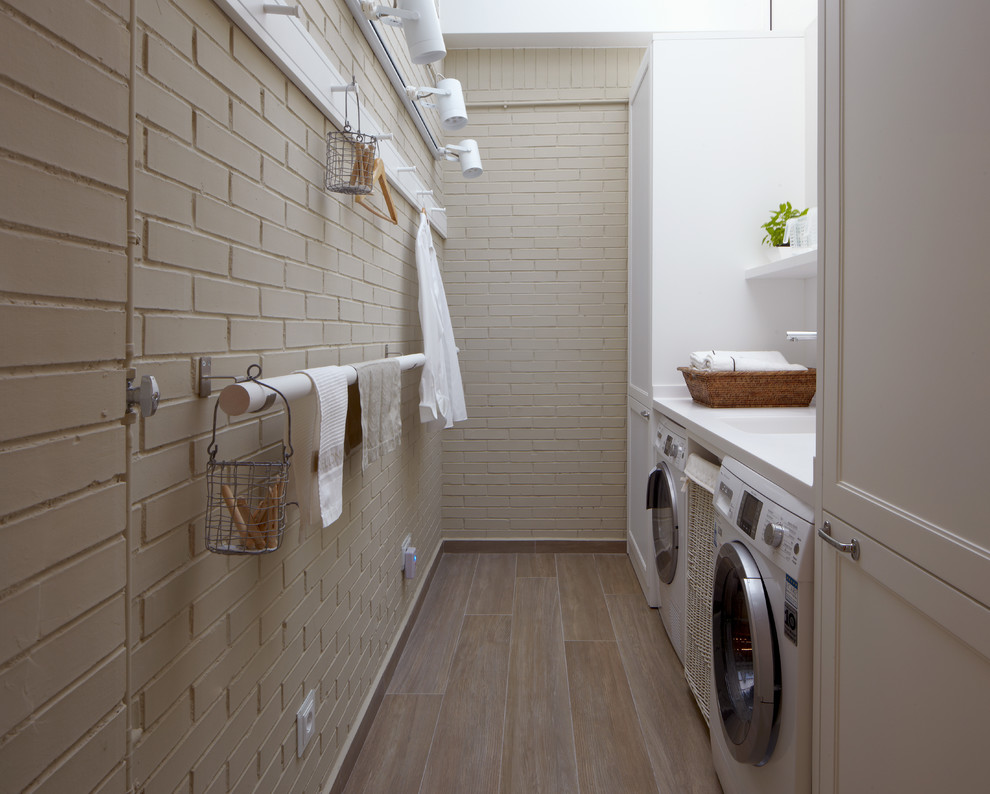 Exempel på en liten industriell beige parallell beige tvättstuga enbart för tvätt, med en integrerad diskho, luckor med infälld panel, vita skåp, bänkskiva i koppar, beige väggar, mellanmörkt trägolv, en tvättmaskin och torktumlare bredvid varandra och beiget golv