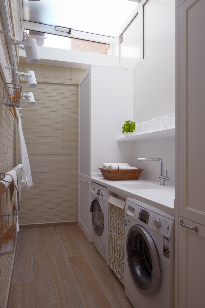 Idéer för att renovera en mellanstor industriell linjär tvättstuga enbart för tvätt, med en enkel diskho, vita väggar, en tvättmaskin och torktumlare bredvid varandra, luckor med infälld panel och vita skåp