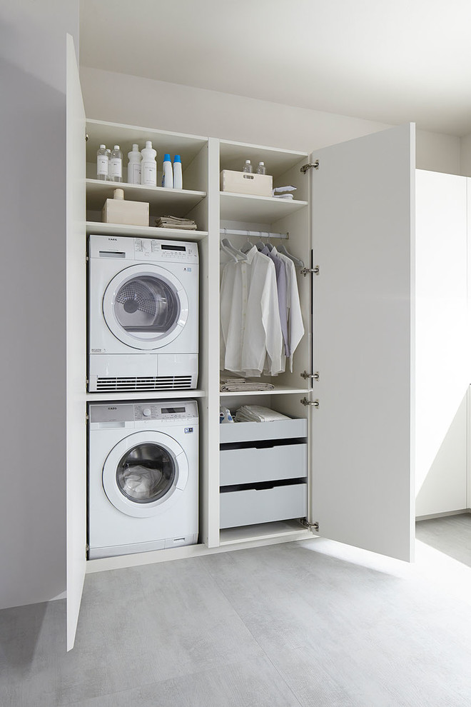 Ejemplo de lavadero lineal actual pequeño con armarios con paneles lisos, puertas de armario blancas, paredes blancas y lavadora y secadora apiladas