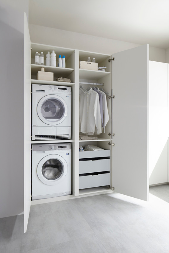 Ejemplo de armario lavadero lineal actual pequeño con armarios con paneles lisos, puertas de armario blancas, paredes blancas y lavadora y secadora apiladas