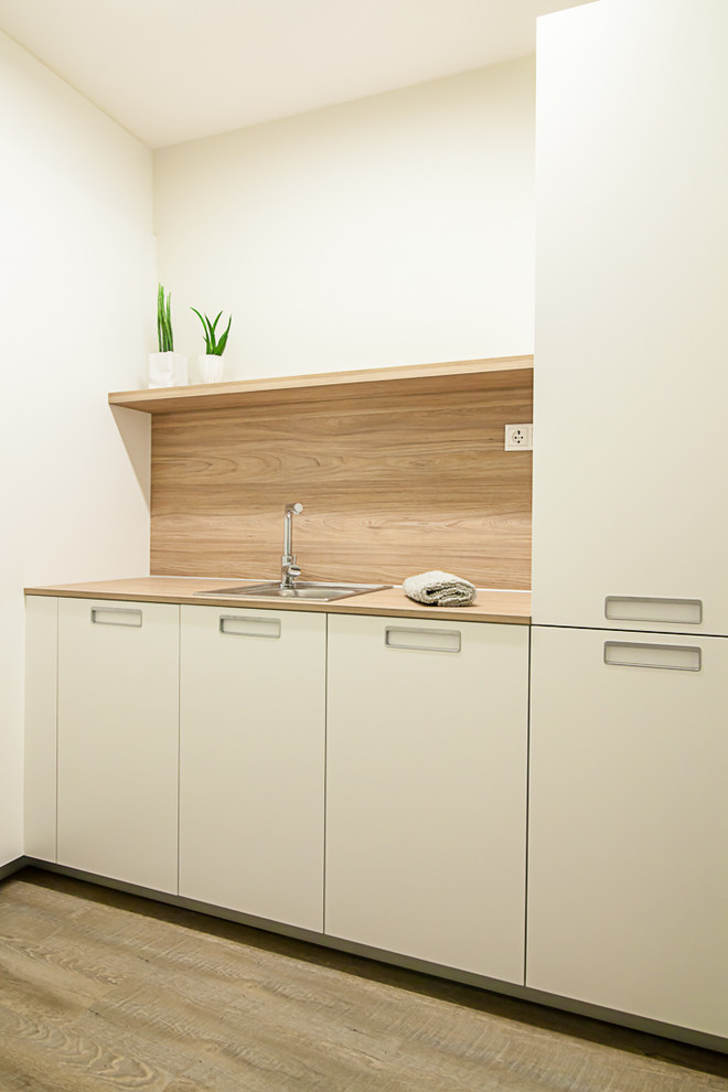 Immagine di una piccola lavanderia multiuso classica con ante lisce, pareti bianche e pavimento in legno massello medio